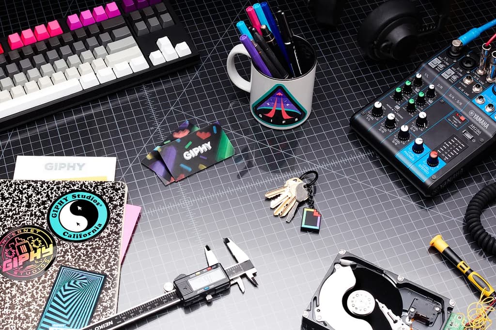 A desk with a notebook, keys (including a GIPHY logo keychain), pens, and a colorful keyboard.